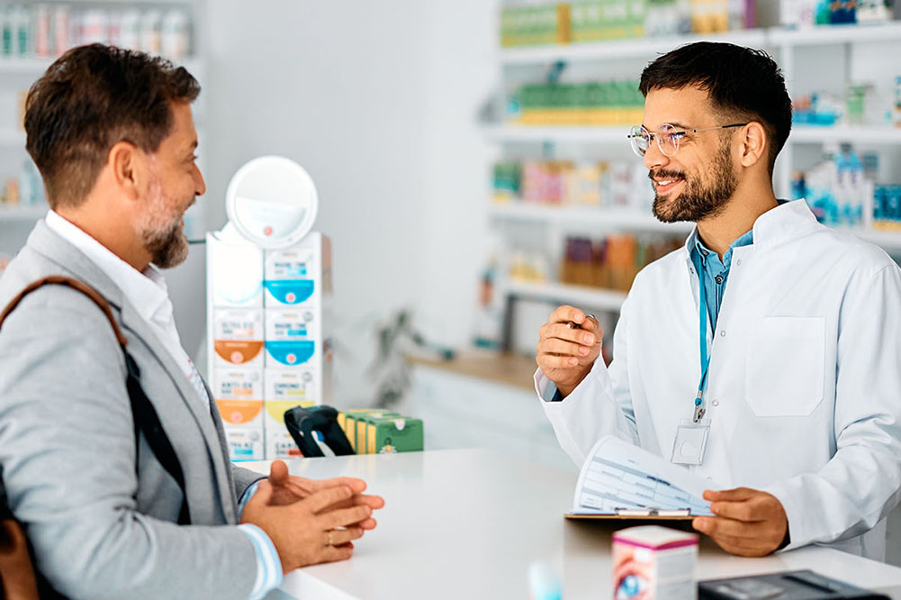 Happy Pharmacist Advising Male Customer In Pharmacy.